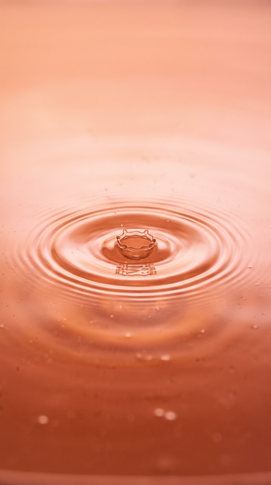 A single peach-coloured drop landing on still water, sending out soft ripples